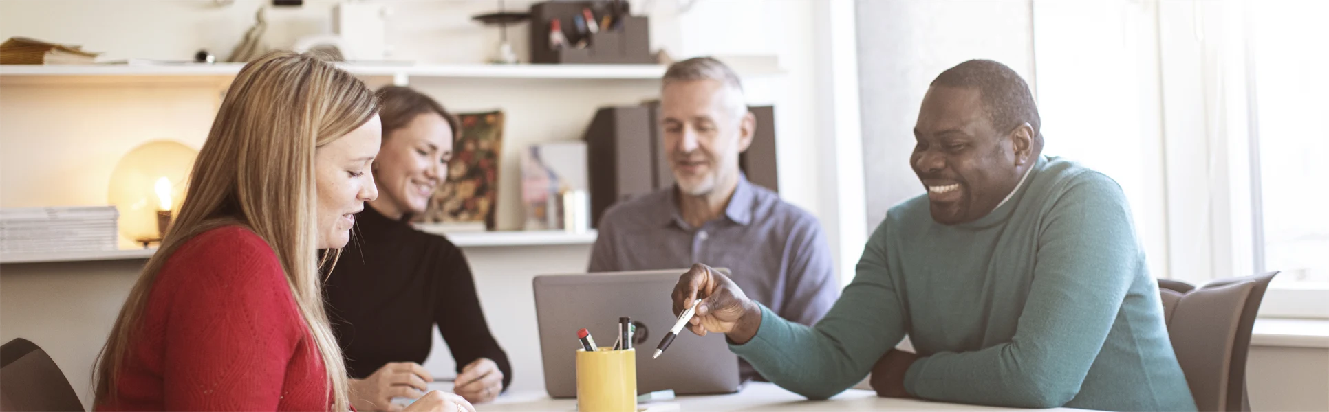 Fyra studenter runt ett bord som arbetar med en laptop och post-it lappar.