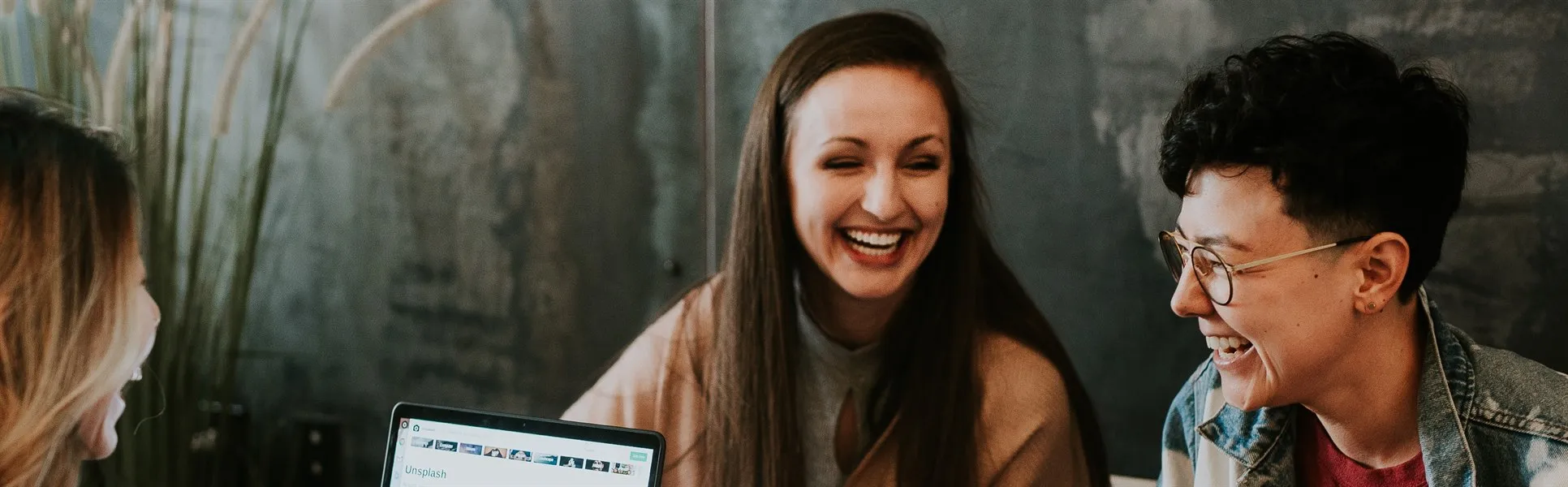  Three people laughing at a table, with computers in front of them