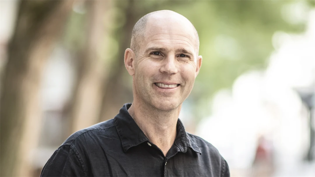 Leende man med svart skjorta tittar in i kameran. 