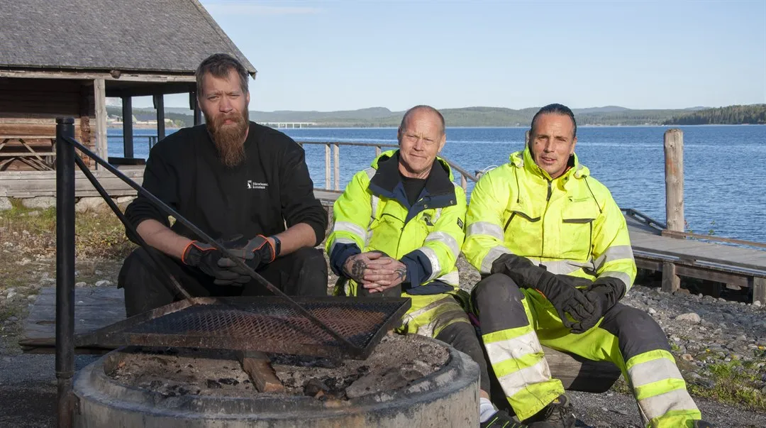 Tre personer sitter utomhus vid en grillplats.