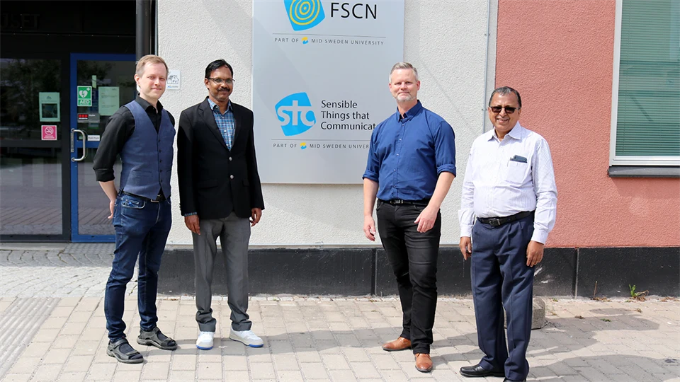 Fyra män som står vid en fasadskylt med texten STC Research Center.