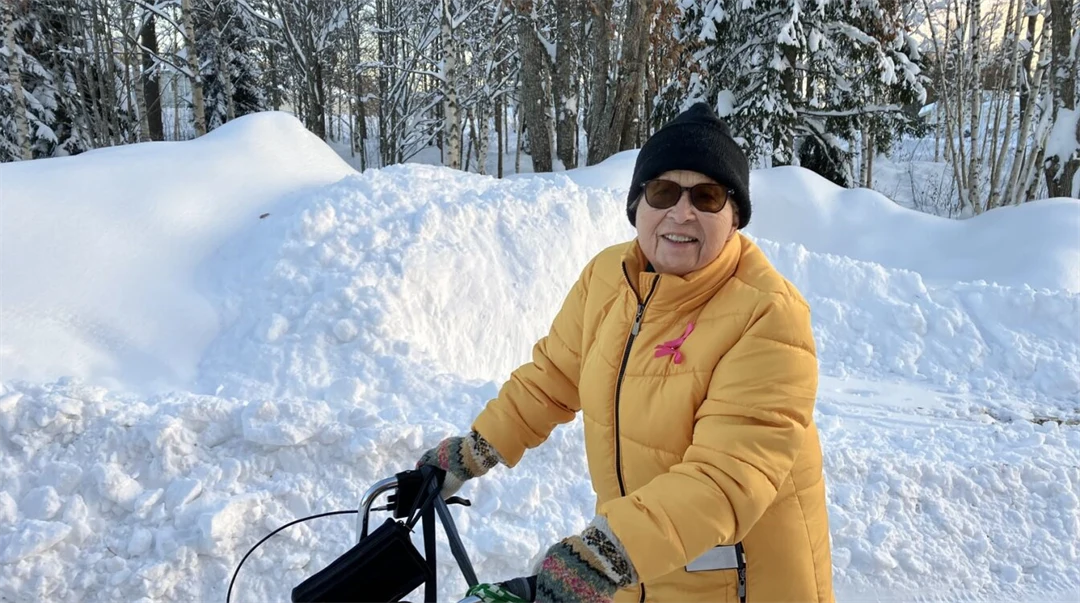 Glad äldre kvinna iklädd varma vinterkläder är ute och promenerar med sin rullator.