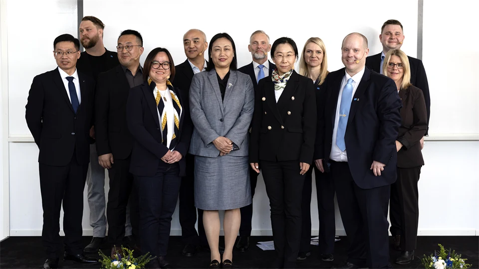 Gruppfoto av män och kvinnor i kostym/dräkt framför vit vägg