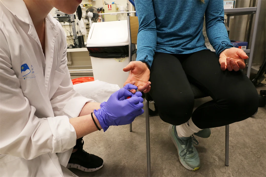 A person in a lab coat takes a blood sample from a person who is sitting.