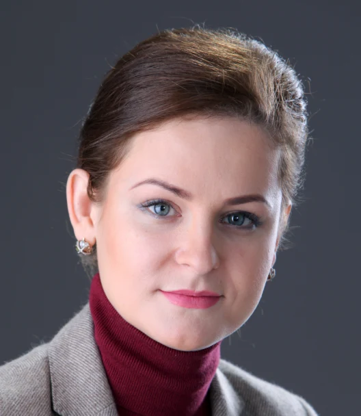 En porträttbild på en kvinna med mörkt uppsatt hår, en vinröd polotröja och grå kavaj