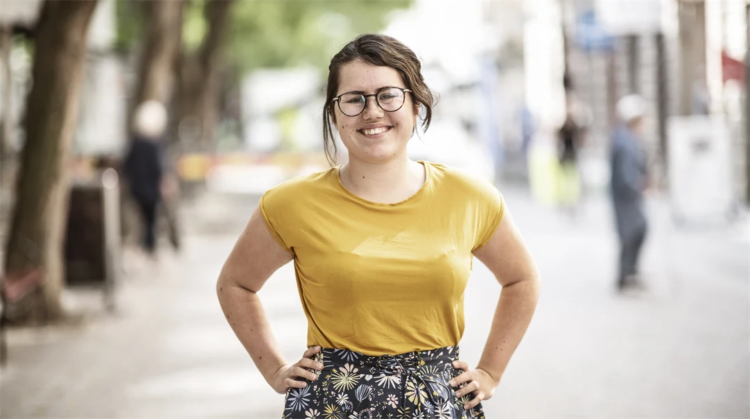 Kvinna med gul topp och mönstrad kjol ler mot kameran 