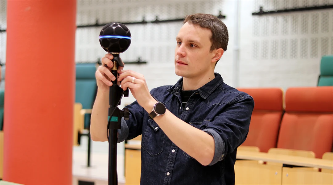 En man som håller i digitalutrustning i en föreläsningssal. 