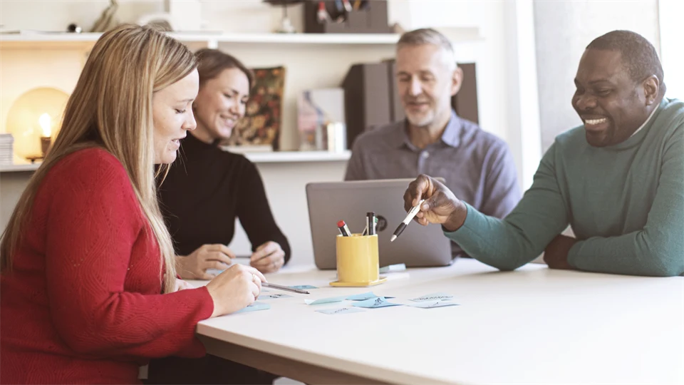 Fyra studenter runt ett bord som arbetar med en laptop och post-it lappar.