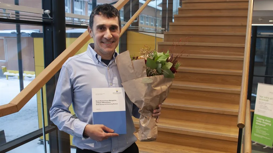 En mörkhårig man poserar för kameran med en blombukett och sin doktorsavhandling.