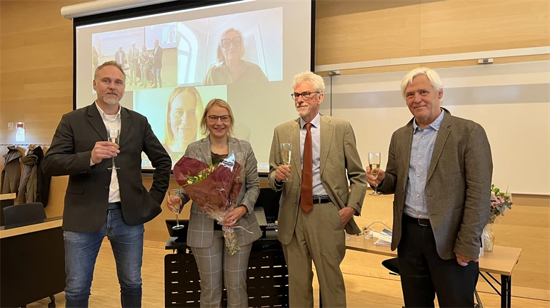 Fyra personer ståendes framför ett skrivbord med glas i handen.